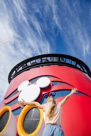 A woman wearing a Minnie Mouse Ear Band standing with raised arms at the base of a funnel on a Disney cruise ship 