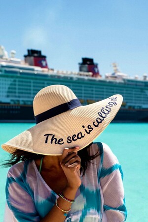 A woman in a straw hat with the words ‘The Sea is Calling’ next to Disney cruise ship
