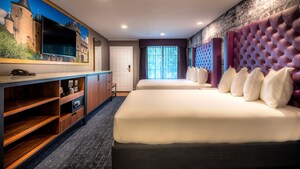 Two queen beds with headboards across from a flat screen TV mounted on a mural of a castle above a long dresser with shelves