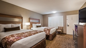 A hotel guest room features 2 queen size beds, a nightstand, and lamp