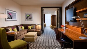 A parlor with a sleeper sofa, easy chair, desk, flat-screen TV and, beyond, open doors to a bedroom