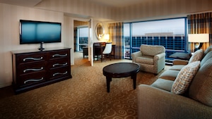 A living room with a TV-dresser, sofa, oval coffee table, easy chair, desk and a large window