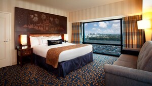 Una cama King Size con una cabecera de Sleeping Beauty Castle frente a un sofá y al lado de una ventana grande