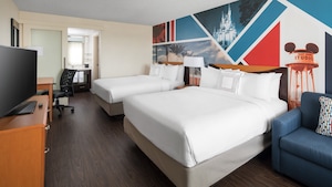 The interior of a room with a sofa, two queen size beds, desk and chair, bureau, flat screen TV and Disney theme park inspired graphics on one wall
