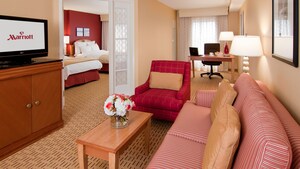 A sofabed, coffee table, TV-cabinet, easy chair and a desk next to a bedroom with 2 double beds