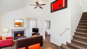 A bi level condo suite features a loft with staircase and a living area with a fireplace, a dinette set and a separate bedroom on the lower floor