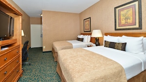 Two double beds with wooden headboards across from a TV dresser, desk and, beyond, a front door