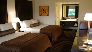 Two beds with bolster pillows and headboards across from a desk and, beyond, a vanity area