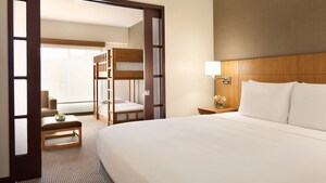 An illuminated family-style suite at Hyatt Place at Anaheim Resort/Convention Center with two sleeping areas featuring a king-sized bed and twin-bunk beds