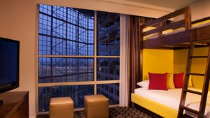 A bunk bed next to a wall of windows and across from a flat screen TV on a dresser