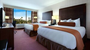 Two queen beds with headboards across from a TV-dresser and a desk and, beyond, a window