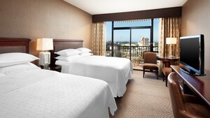 Two queen beds across from a desk-TV-dresser and, beyond, 2 easy chairs and a balcony