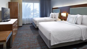 Queen suite bedroom with 2 queen beds, nightstand and lamp, across from a dresser with television and armoire
