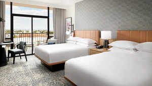 Dos camas queen frente a una mesa y un balcón