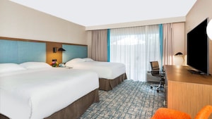 A room at The Anaheim Hotel with a dresser, desk, TV, nightstand, 2 chairs and 2 beds