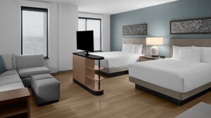 The Studio Kitchen Suite, with an L shaped couch and ottoman facing a flat screen TV, and 2 queen beds