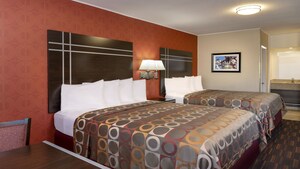 A hotel bedroom with a table, 2 beds and a sink