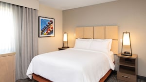 A 1 bedroom queen suite from Candlewood Suites Anaheim Resort Area featuring a bed, 2 side tables, 2 lamps and hanging artwork