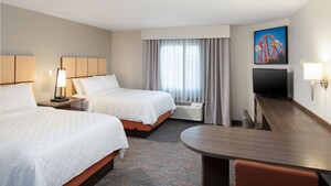 The Studio Suite at Candlewood Suites Anaheim Resort Area featuring 2 beds, a side table, a lamp, a TV, a desk, 2 chairs and hanging artwork
