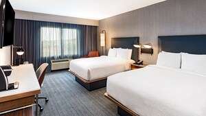 A guest room that includes 2 queen beds, a desk and a television mounted on the wall.