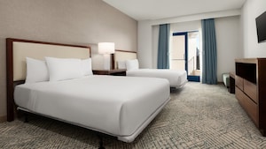 A hotel bedroom with 2 queen size beds, nightstand, TV, dresser and a glass door with balcony access