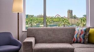 A Deluxe View Studio Suite with a couch, chair and standing lamp, and a view of Disney California Adventure Park.
