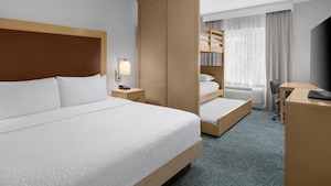A hotel resort suite bedroom with a bed, dresser, desk, TV and a bunk bed with 3 mattresses