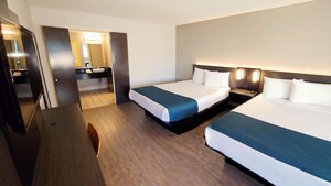 A hotel bedroom with 2 queen size beds, a night stand, TV and doors leading to a private bathroom