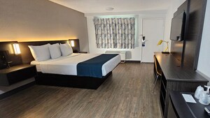 A queen bed, 2 end tables and a desk, with drawn curtains on a window