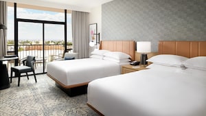 Two queen beds across from a table and balcony