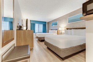 A hotel bedroom with a bench, mirror, dresser, TV, microwave and 2 beds