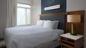 A king bed planked by a medium-sized window and an end table, with a wallcovering above