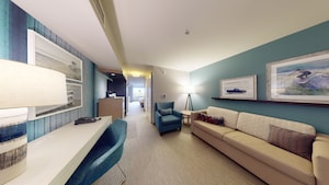 The living room of the King Suite, with an armchair, a long couch and desk, and beach themed pictures on the wall