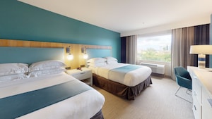 A bright room with 2 queen beds and a dresser, desk, chair and large window