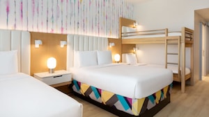 Two standard queen beds with a nightstand with a clock and wall mounted lights between them