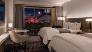 A hotel room at the Westin Anaheim Resort with a table, TV, 2 queen beds, 2 chairs and a balcony with a view of fireworks over Disney California Adventure Park
