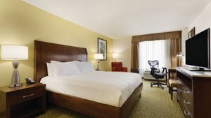 A hotel room with a king-size bed, seating area, desk, desk chair, dresser and flat-screen TV