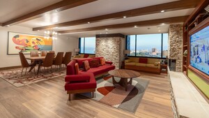 A common area with 3 sofas, a low table, a dining table, an entertainment center with TV and a fireplace in The Incredibles Suite at Pixar Place Hotel