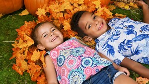 2 young kids laying on a pile of leaves near a bunch of pumpkins