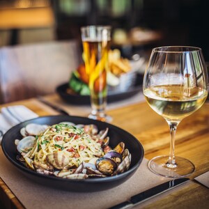 Uma tigela de macarrão e conchas de mariscos perto de uma taça de vinho branco	