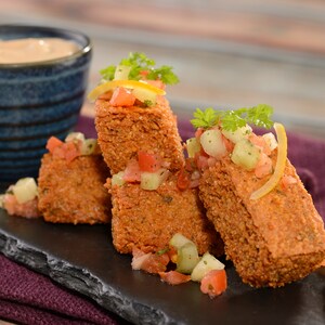 Um prato de homus frito com cobertura de coentro e legumes picados, servido com molho de acompanhamento