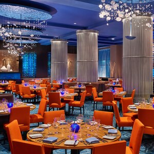 Um restaurante moderno com mesas postas de modo formal, booths, colunas decorativas e lustres abstratos que remetem a bolhas embaixo d’água