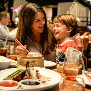 Mãe e  crianças sorriem enquanto saboreiam seus pratos em um moderno salão de jantar no Morimoto Asia