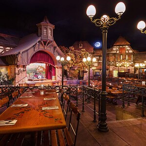 Área de refeições do Biergarten Restaurant com decoração da Bavária, grandes mesas compartilhadas, postes de iluminação e um palco