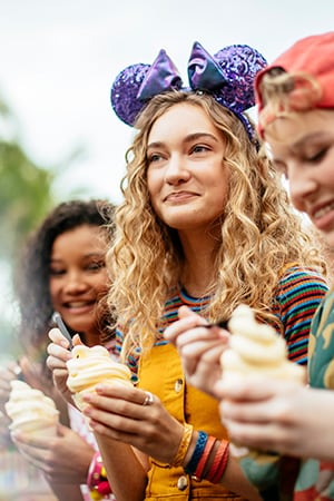 A woman in a Minnie Mouse ear hat eats a bowl of ice cream with two friends