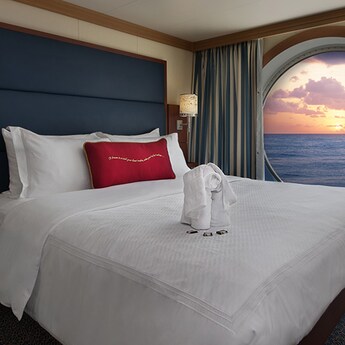 Uma cabine com a janela voltada para o mar e uma cama com toalhas dobradas