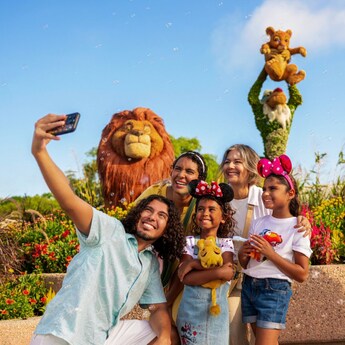 A family of 5 crowding together for a selfie in front of topiary versions of characters from The Lion King