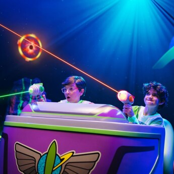 Two young Guests taking aim with their lazer blasters while riding Buzz Lightyear's Space Ranger Spin at Magic Kingdom park