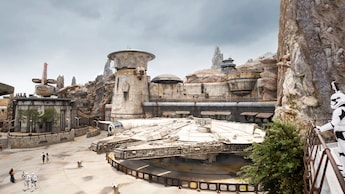 Un Stormtrooper de la Primera Orden vigila el Millennium Falcon atracado cerca de edificios exóticos de Star Wars y torres de madera petrificada