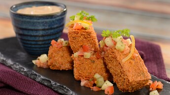 A plate of hummus fries topped with cilantro and chopped vegetables, served with a dipping sauce